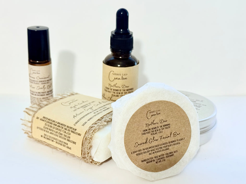 Spirit Led Creative products including Northern Dew dry hair oil, Sacred Glow Facial Bar, Agate Gardens Sugar Scrub Bar, and Scalp oil displayed on natural wooden surface | Small batch, Michigan made